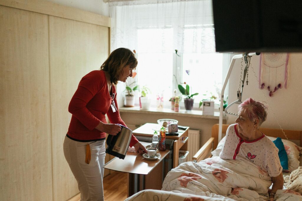 A caregiver serves tea to a senior woman in a cozy bedroom setting, fostering comfort and care.